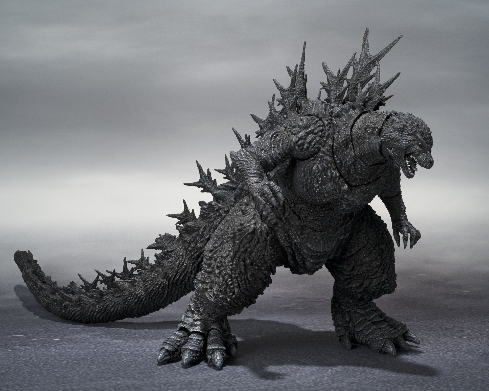 Angled view of Godzilla Minus One figure displaying back spikes and detailed tail sculpt, left-side perspective.